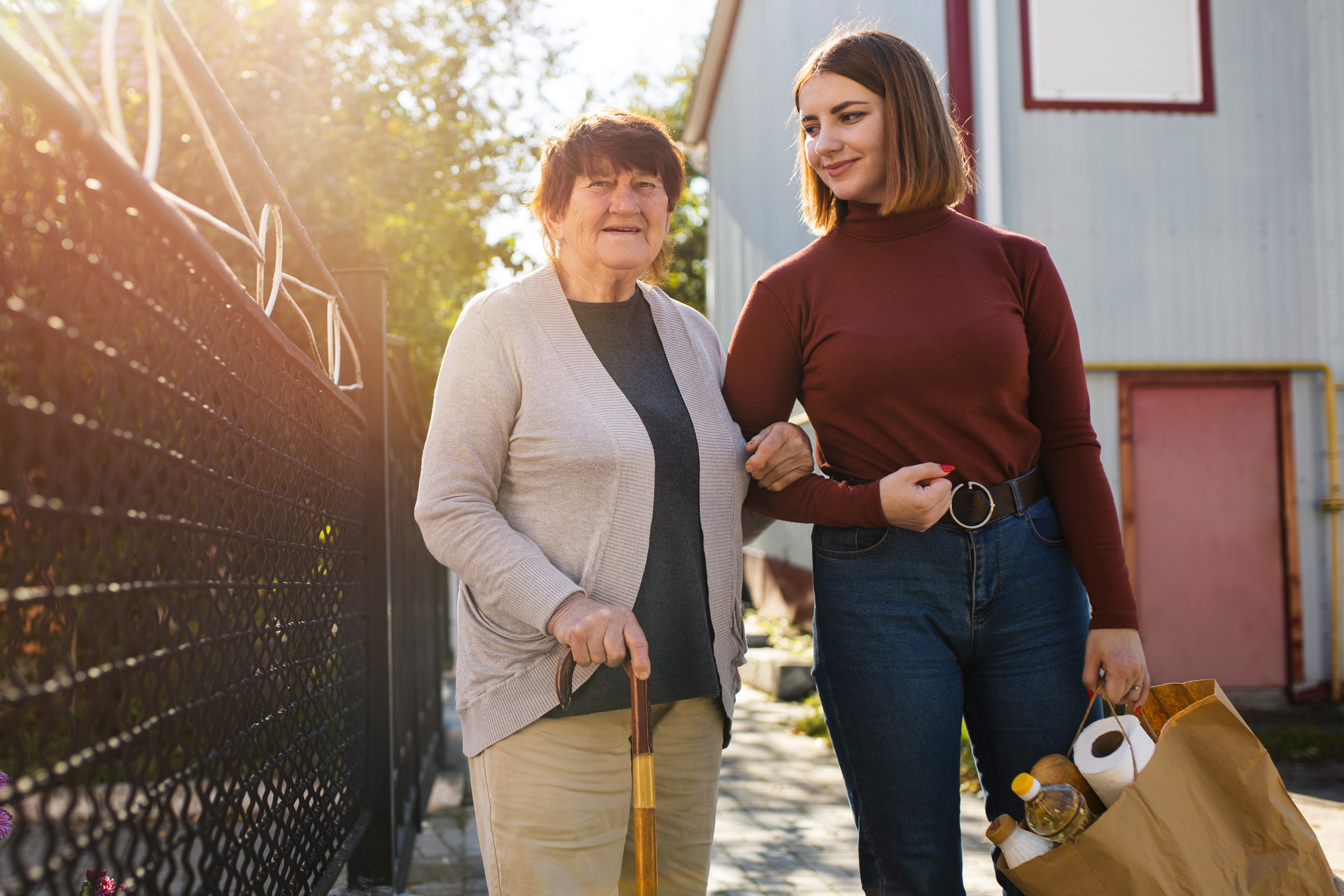 Caregiver assisting elderly woman walking outside