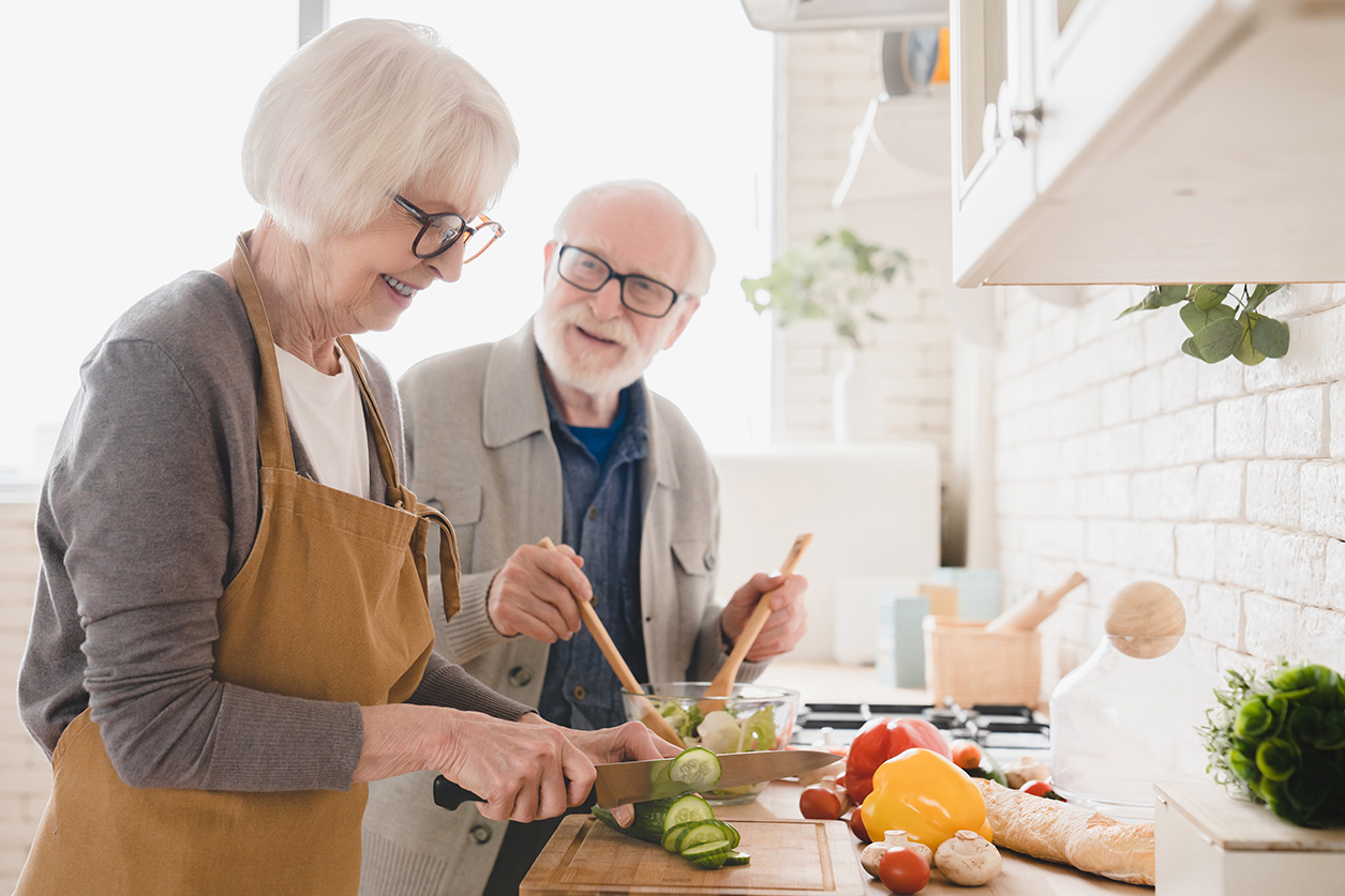 Elderly woman smiling while having a nutritious meal at home, supported by a caregiver.