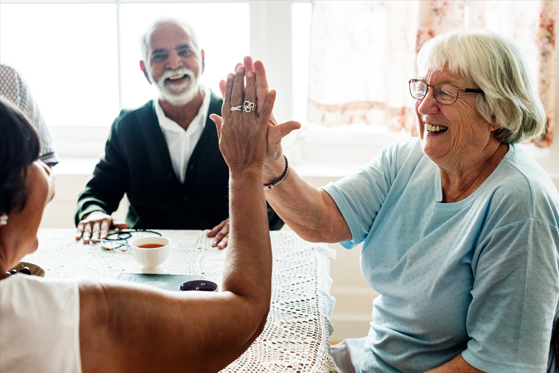 A happy elderly woman high-fives her caregiver in a brightly lit living room.